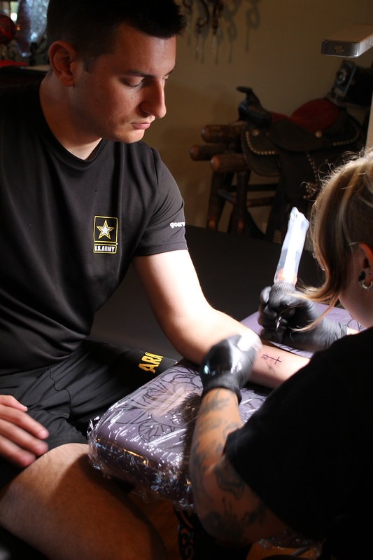 U.S. Army veteran in PT shirt receiving custom commemorative forearm tattoo