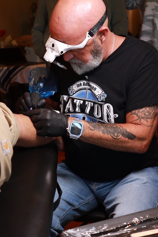 Master Ink Addiction tattoo artist with magnifying visor at work on a participant's arm