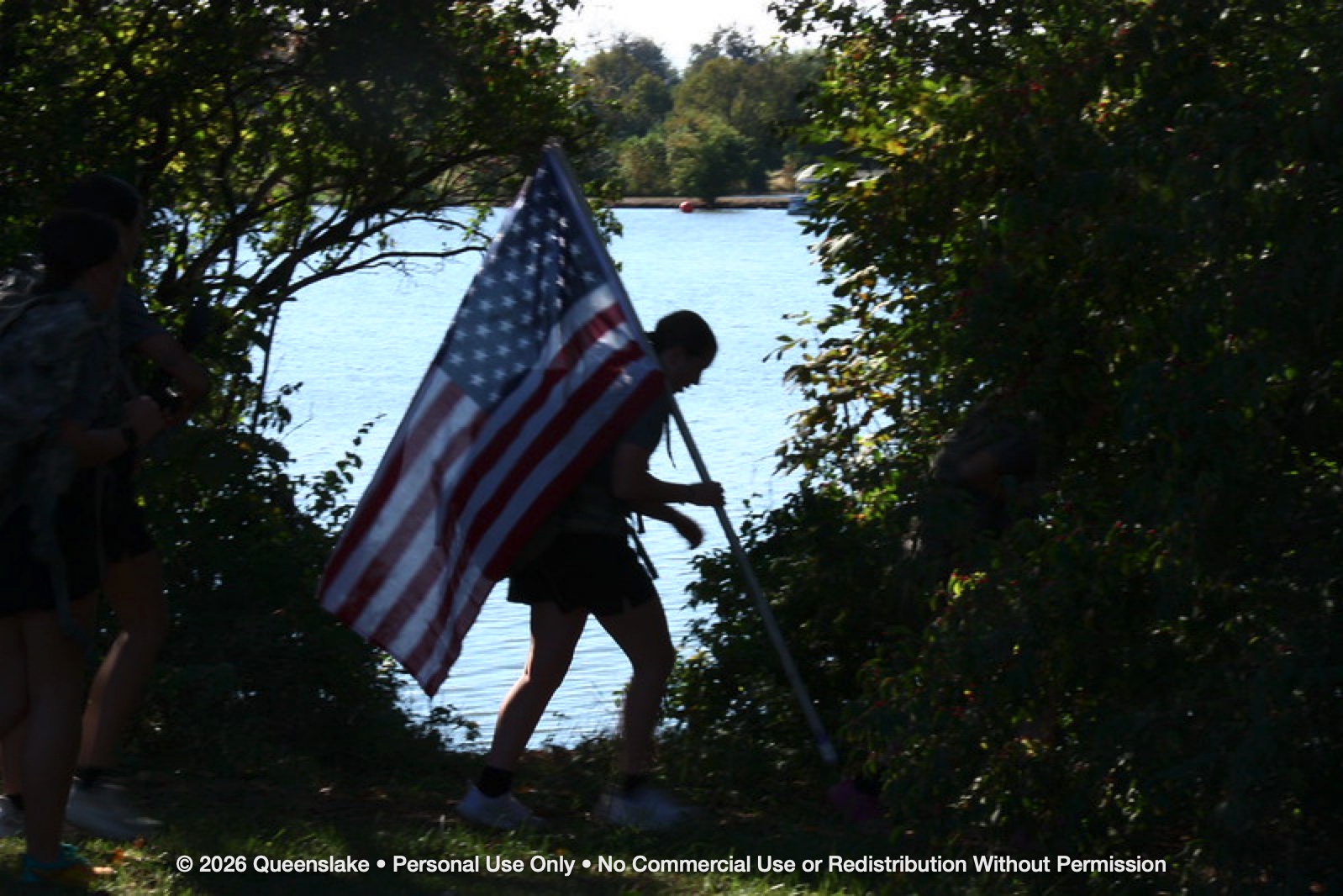 2026 Athlete Carrying American Flag Along Wooded Waterfront Trail